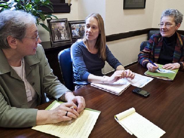 Three individuals sitting a desk with paper talking