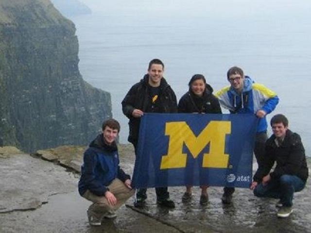 Students posing with a Michigan flag near the edge of a cliff
